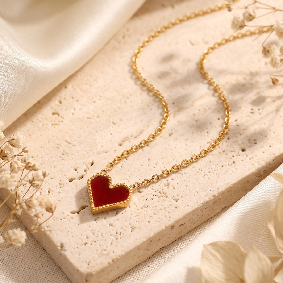 Macro view of the scarlet heart pendant with a gold beaded border on a stone surface.