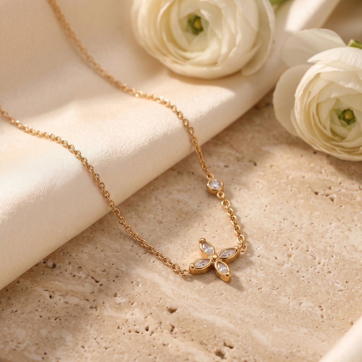 Overhead view of the gold-tone flower necklace laid on a cream stone surface and folded silk fabric.