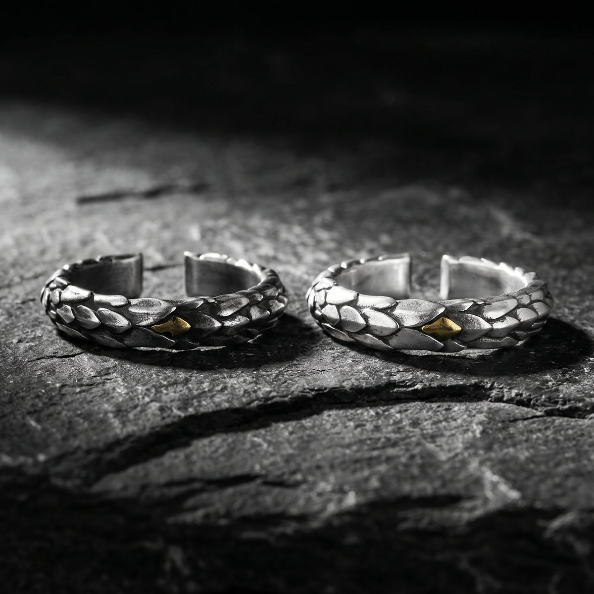 Two dragon-scale open rings with gold-colored accents shown horizontally on dark slate.