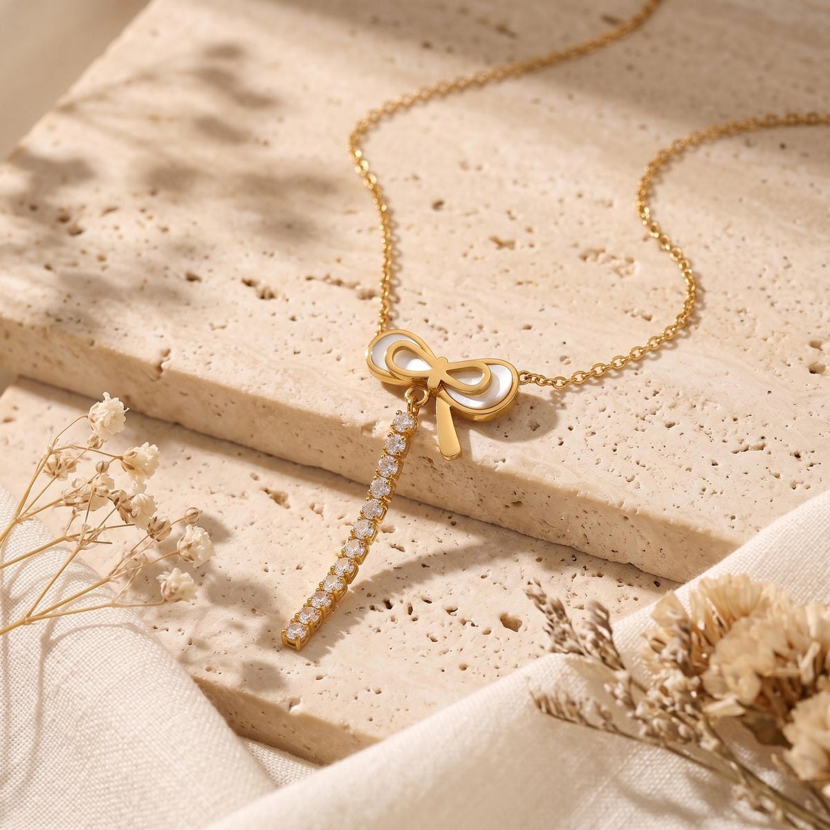 Close-up of the pearlescent gold-tone bow pendant and cascading clear stones on a textured stone surface.