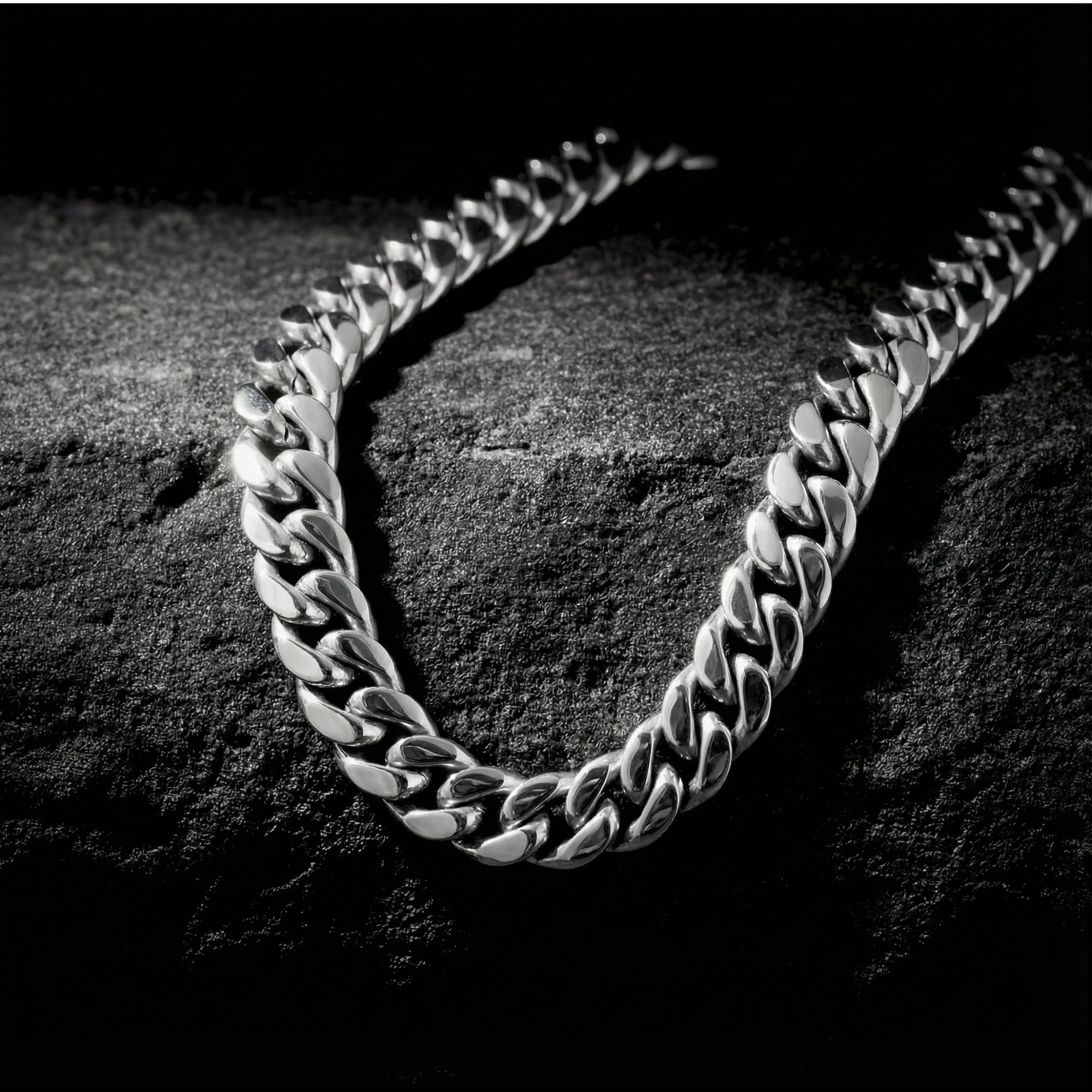 Detailed view of a 12mm silver stainless steel Cuban link chain necklace on a dark stone surface.