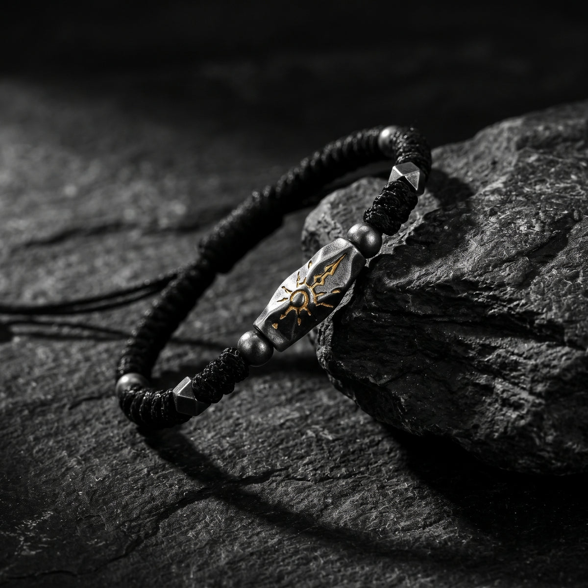 Angled sunburst rope bracelet resting across dark textured rocks, highlighting the carved focal station and braided cord.
