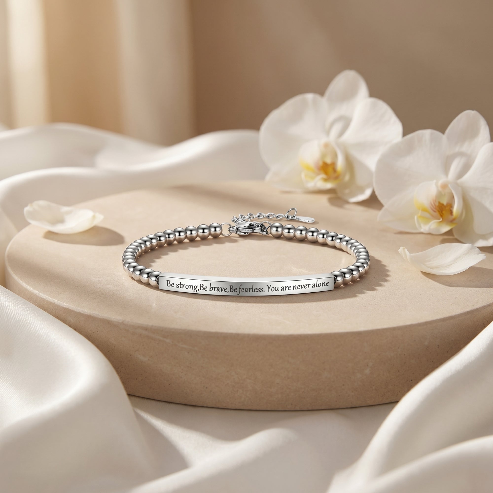 Silver beaded bar bracelet with inspirational engraving on a stone pedestal with flowers.