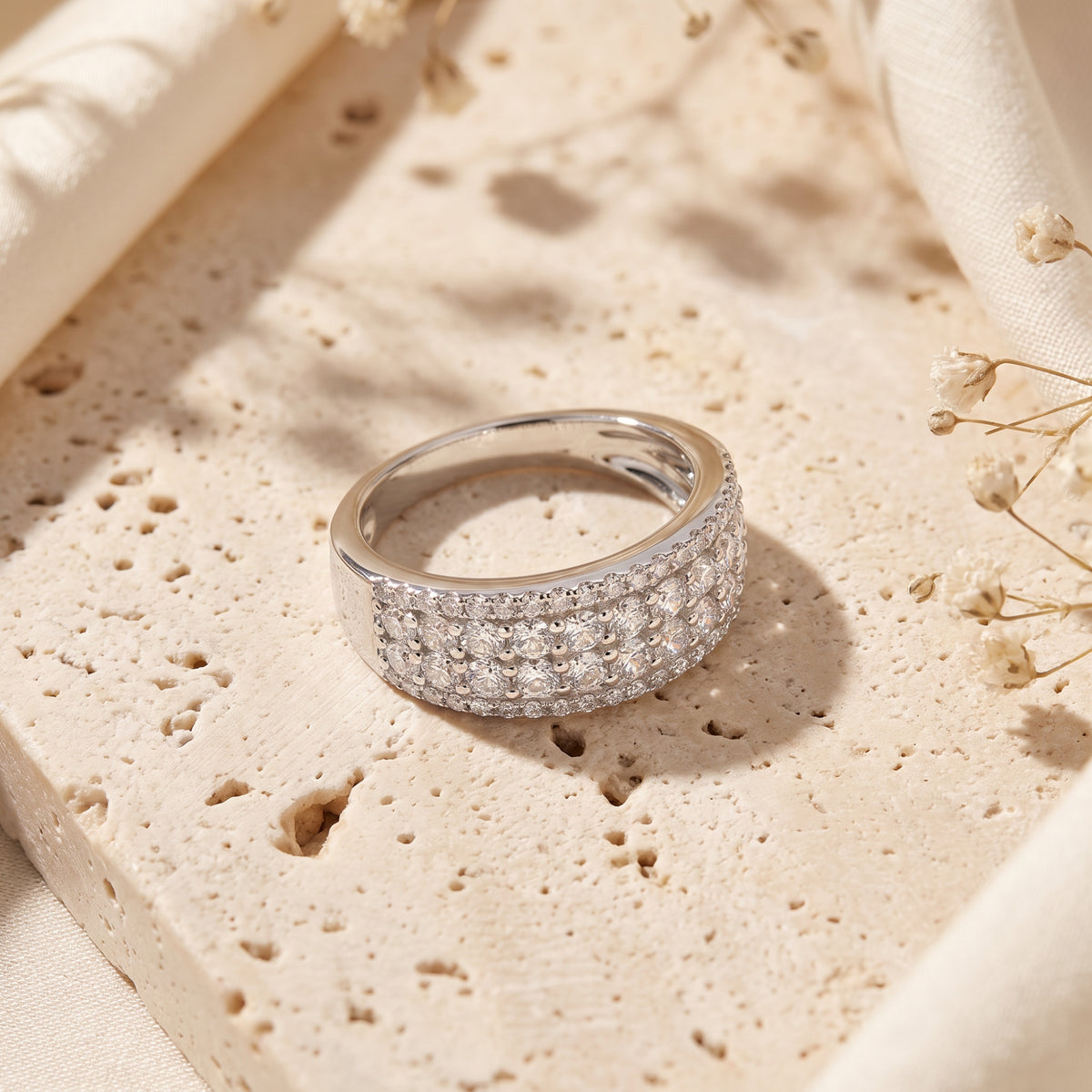 Detail view of a sterling silver wide band ring with rows of round cubic zirconia on a stone background.