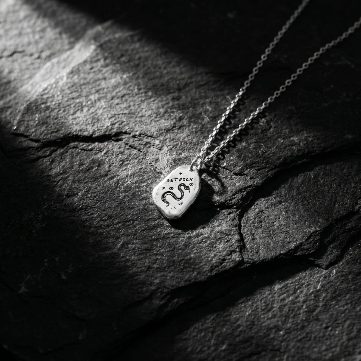 Silver snake pendant necklace lying diagonally on textured dark slate.