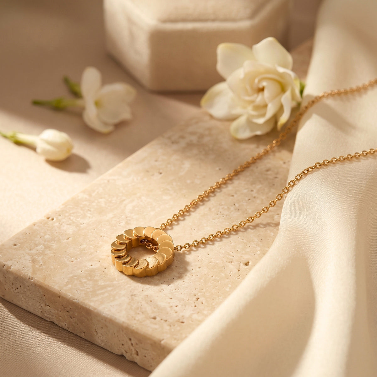 Close-up of the Freya necklace's 18K gold plated overlapping disk pendant on a stone surface.