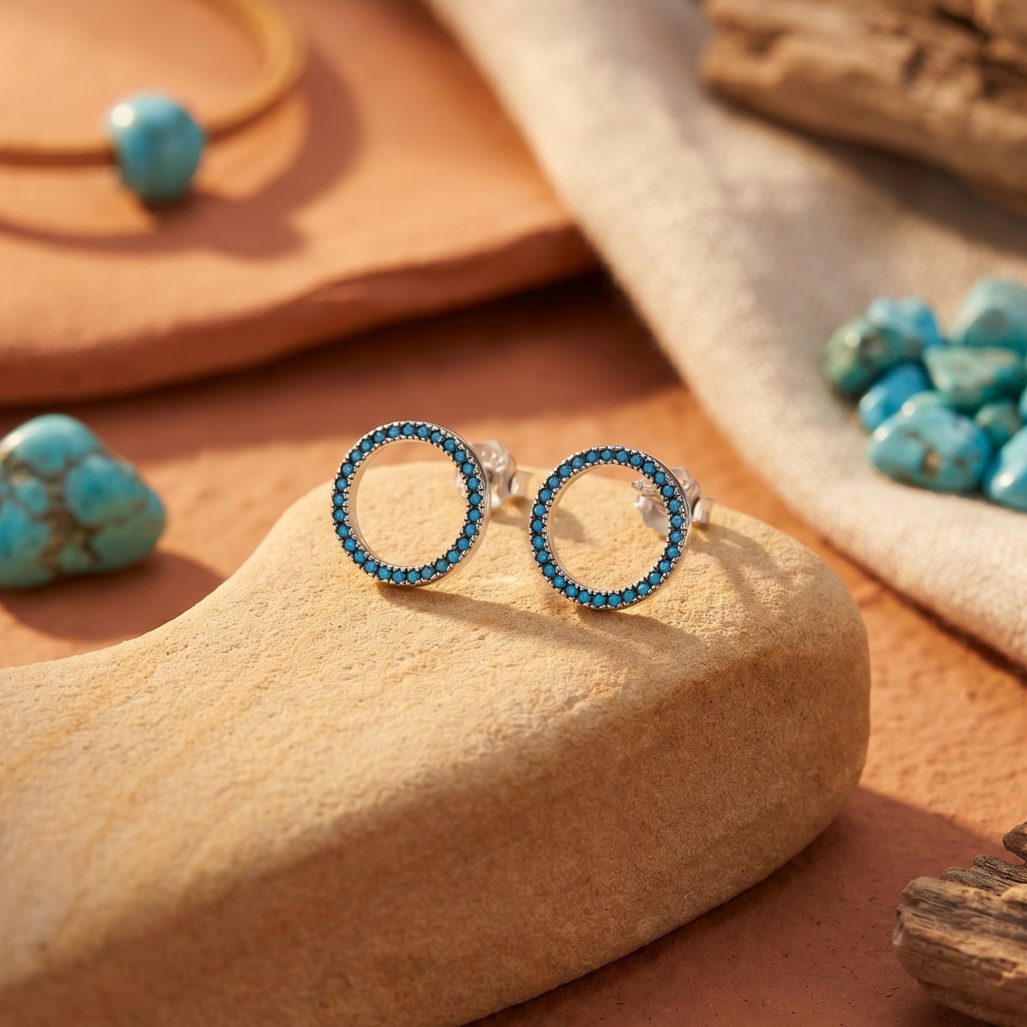 Detail view of silver circle stud earrings featuring a halo of round turquoise stones on a desert stone.