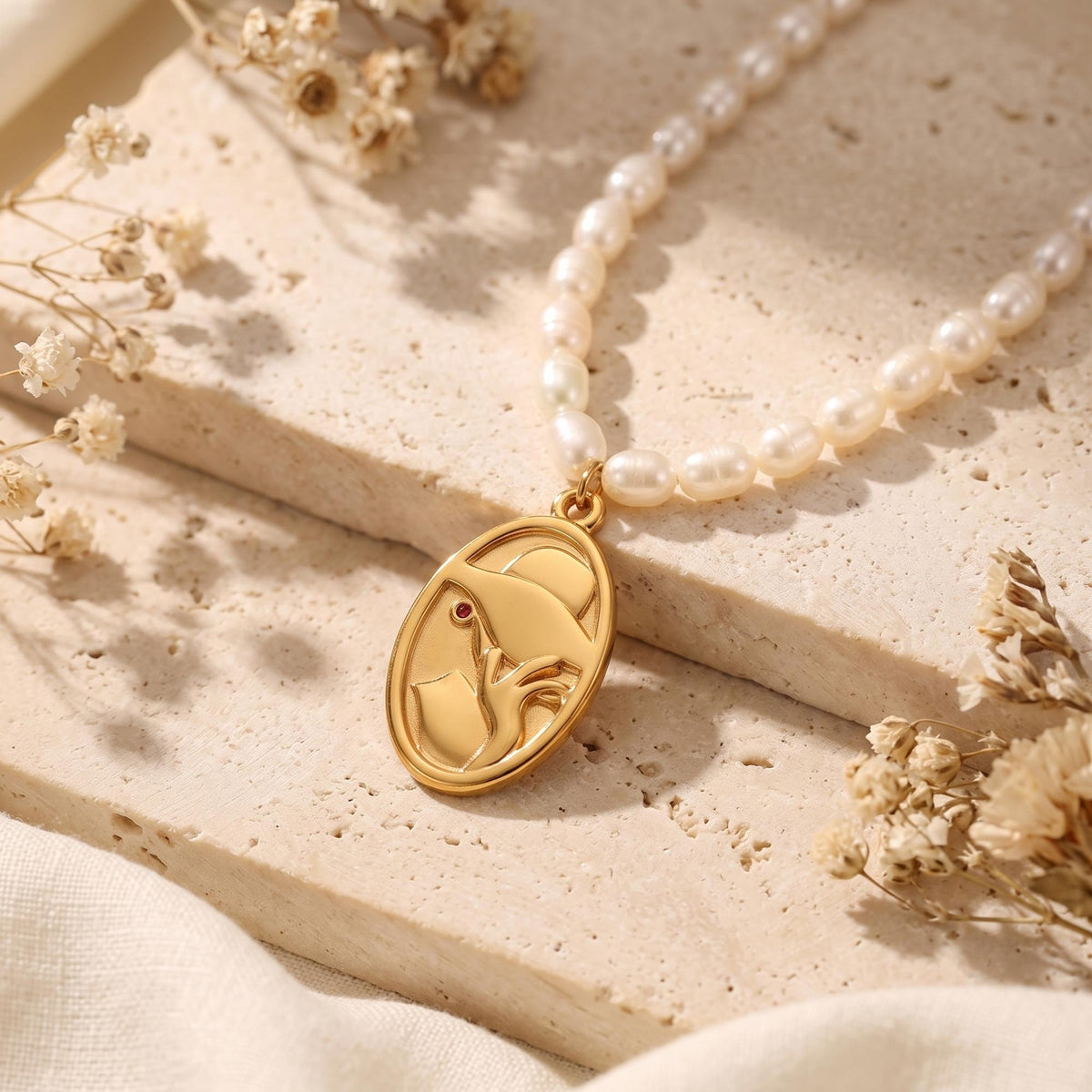 White pearl necklace with a gold-tone oval face-profile pendant worn at the collarbone.