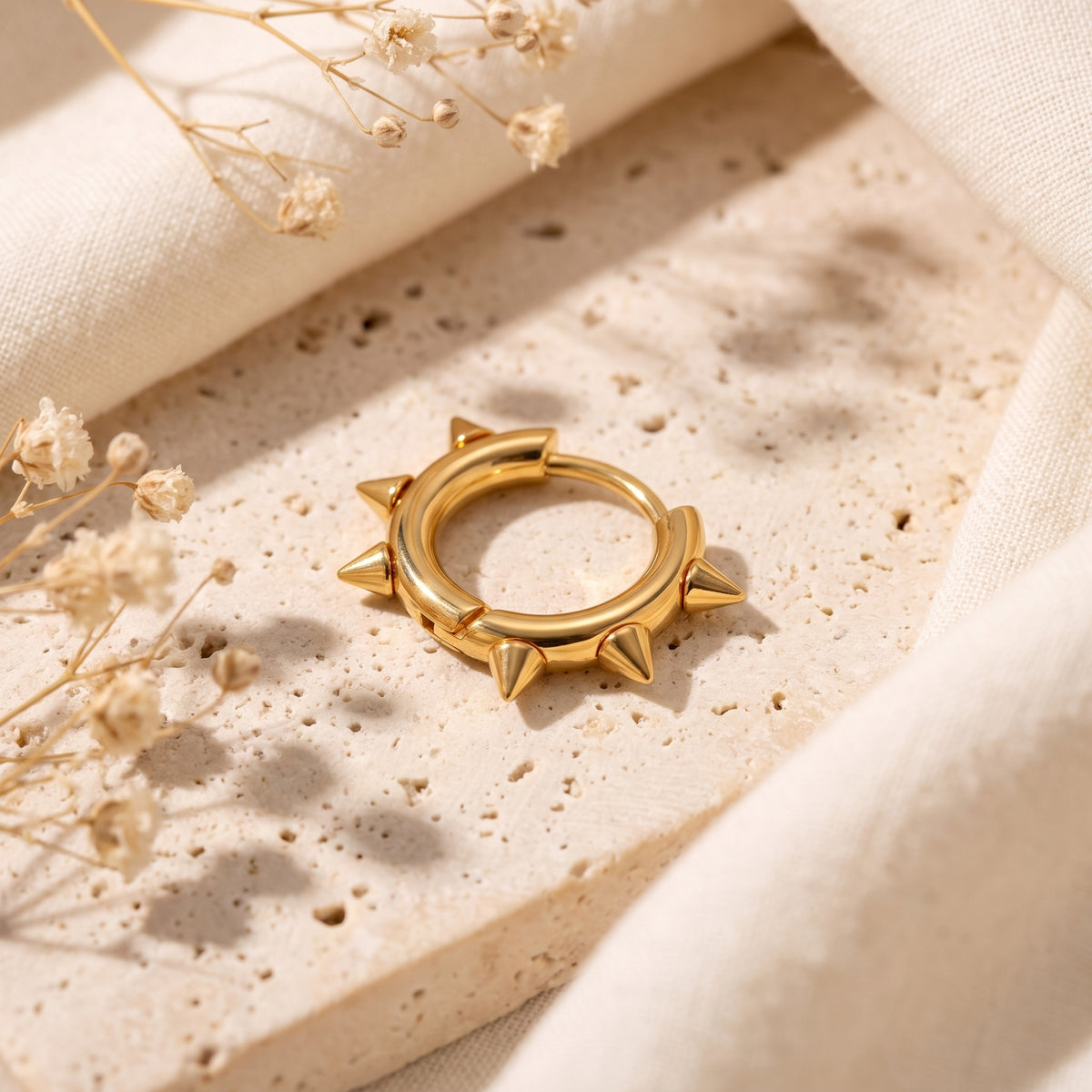Single gold-color spiked hoop earring displayed at an angle on a light beige stone surface.