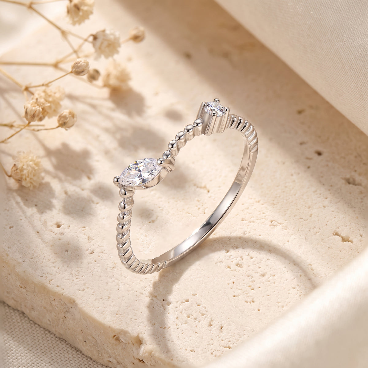 Angled view of the silver beaded bypass ring with marquise and round stones standing on a beige stone slab.