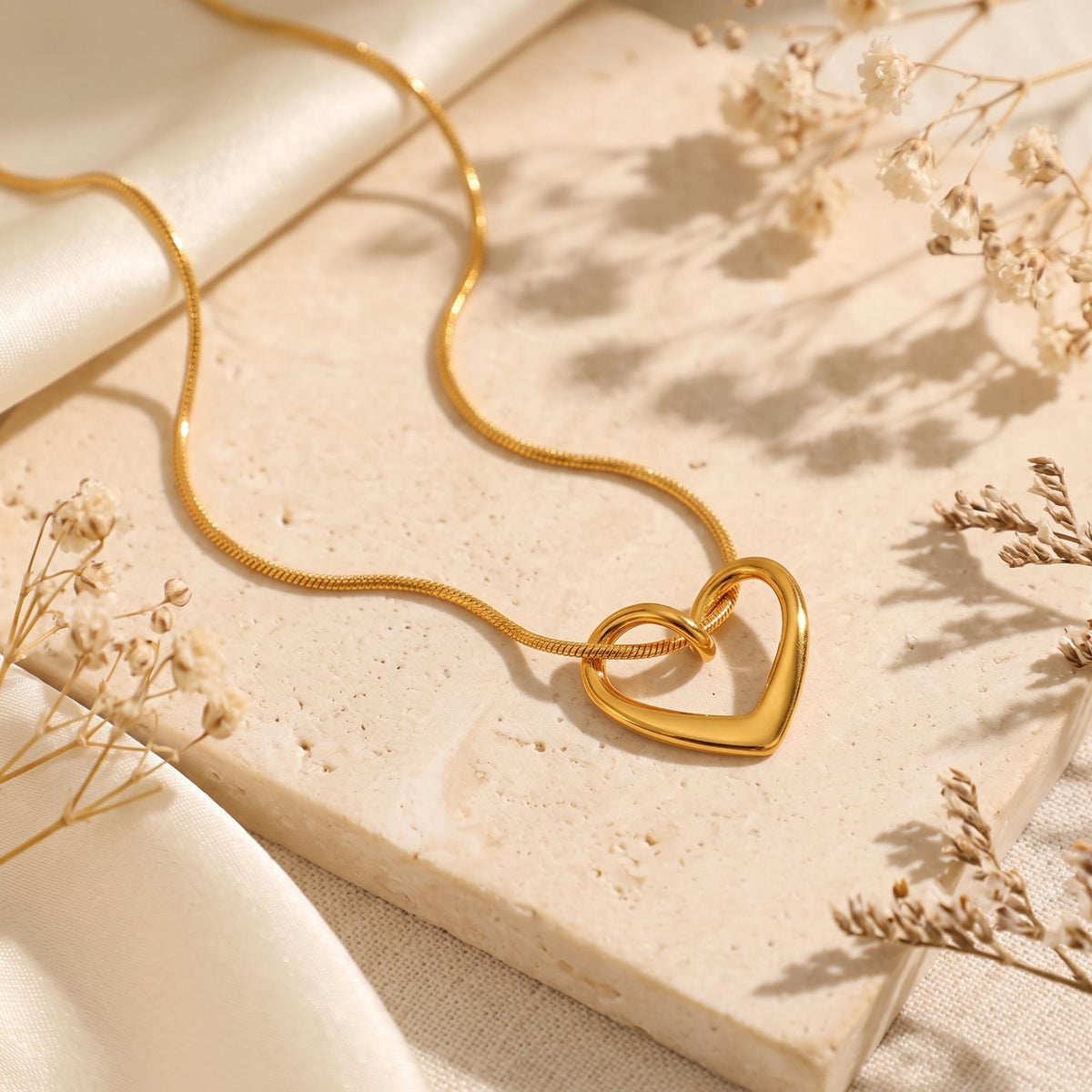 Flat lay view of the gold-tone fluid heart necklace on a snake chain over a textured stone slab.