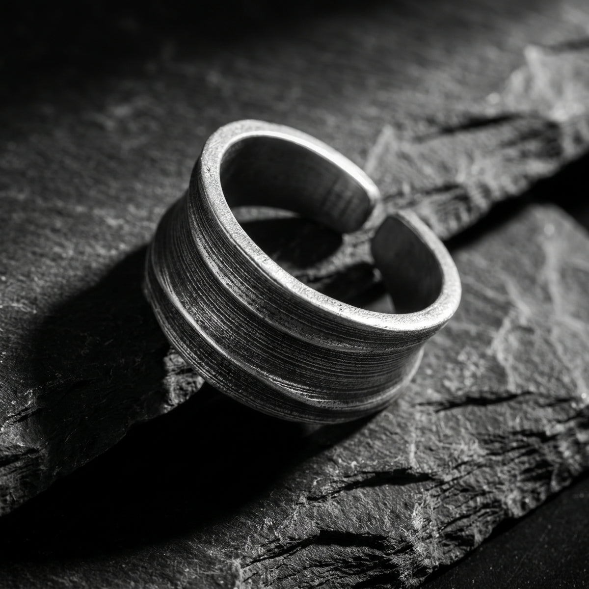 Angled close-up of a silver concave ribbed ring on slate, showing its open band.