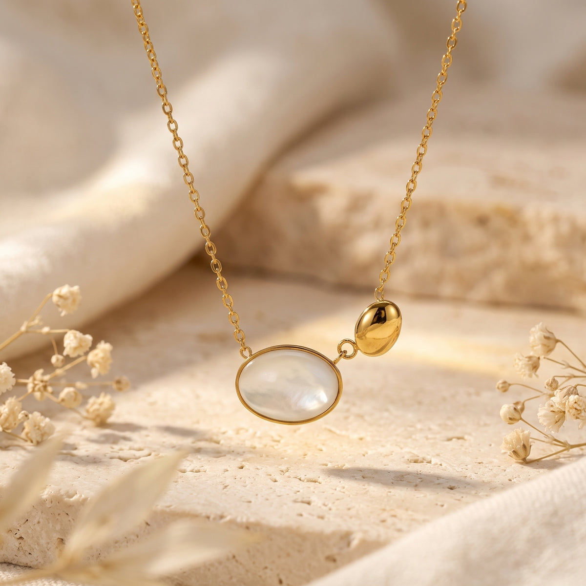 Close-up of a suspended gold-tone necklace with a luminous mother-of-pearl oval and smooth pebble pendant.