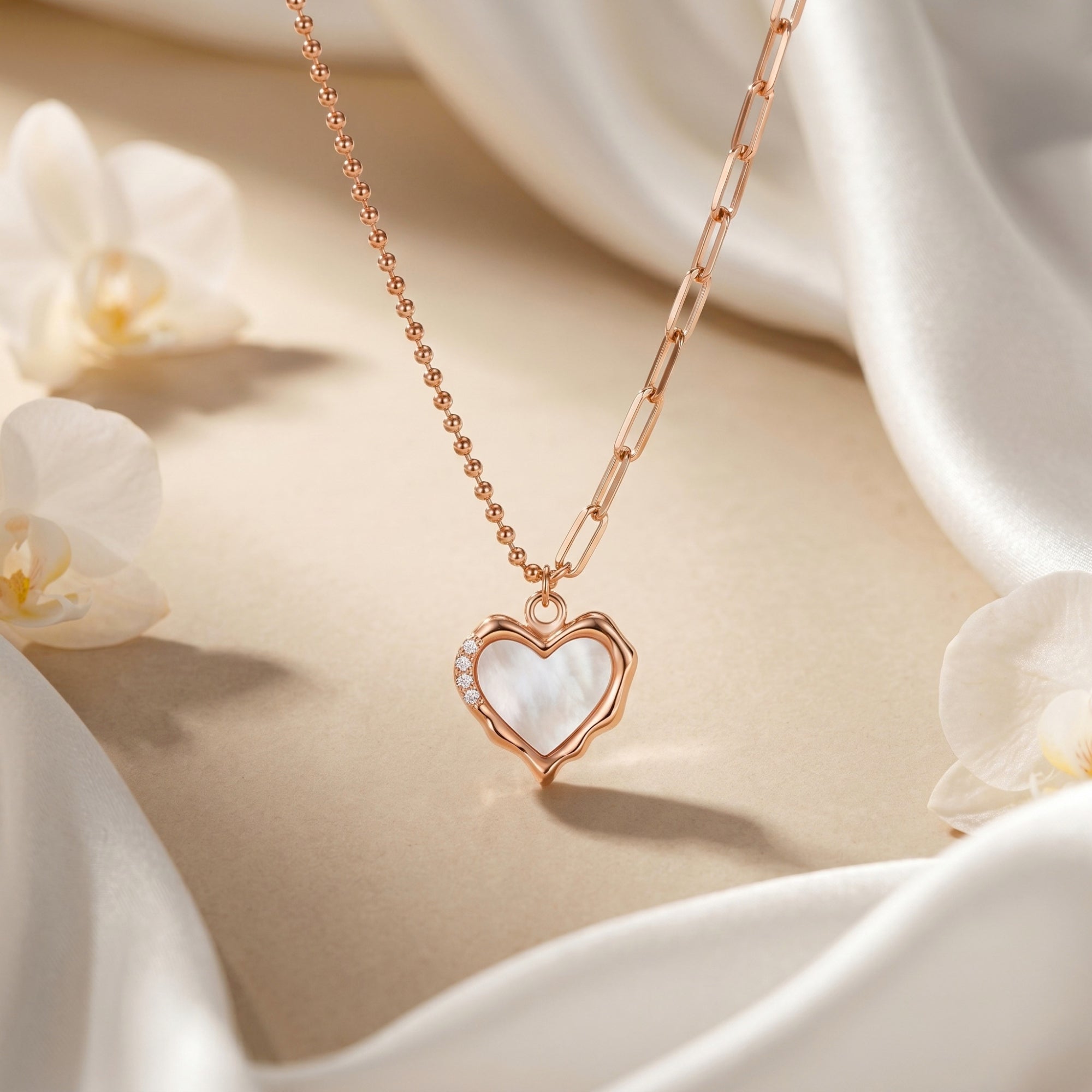 Rose gold heart necklace with white opal pendant displayed against white silk and flowers.