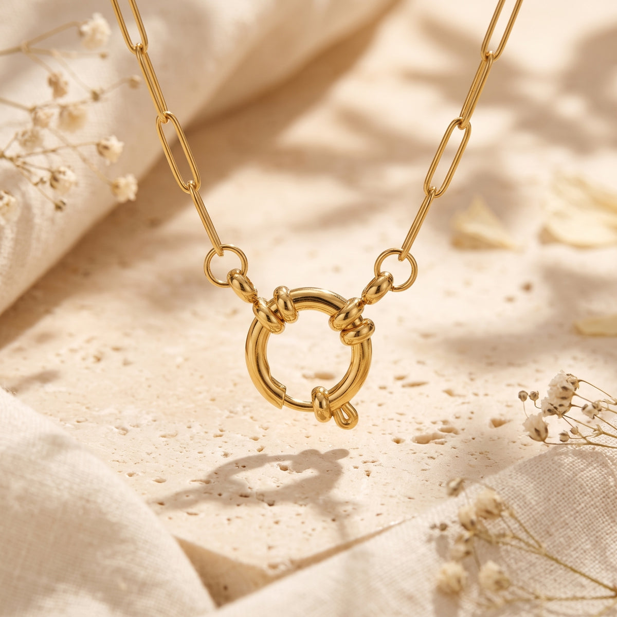 Close-up of the gold-tone paperclip chain and circular sailor spring lock clasp on textured stone.