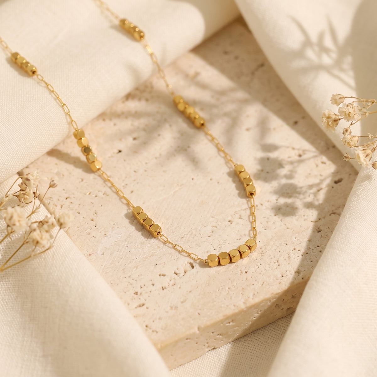 Flat-lay view of the gold-tone station necklace with small cube bead clusters on a textured stone surface.