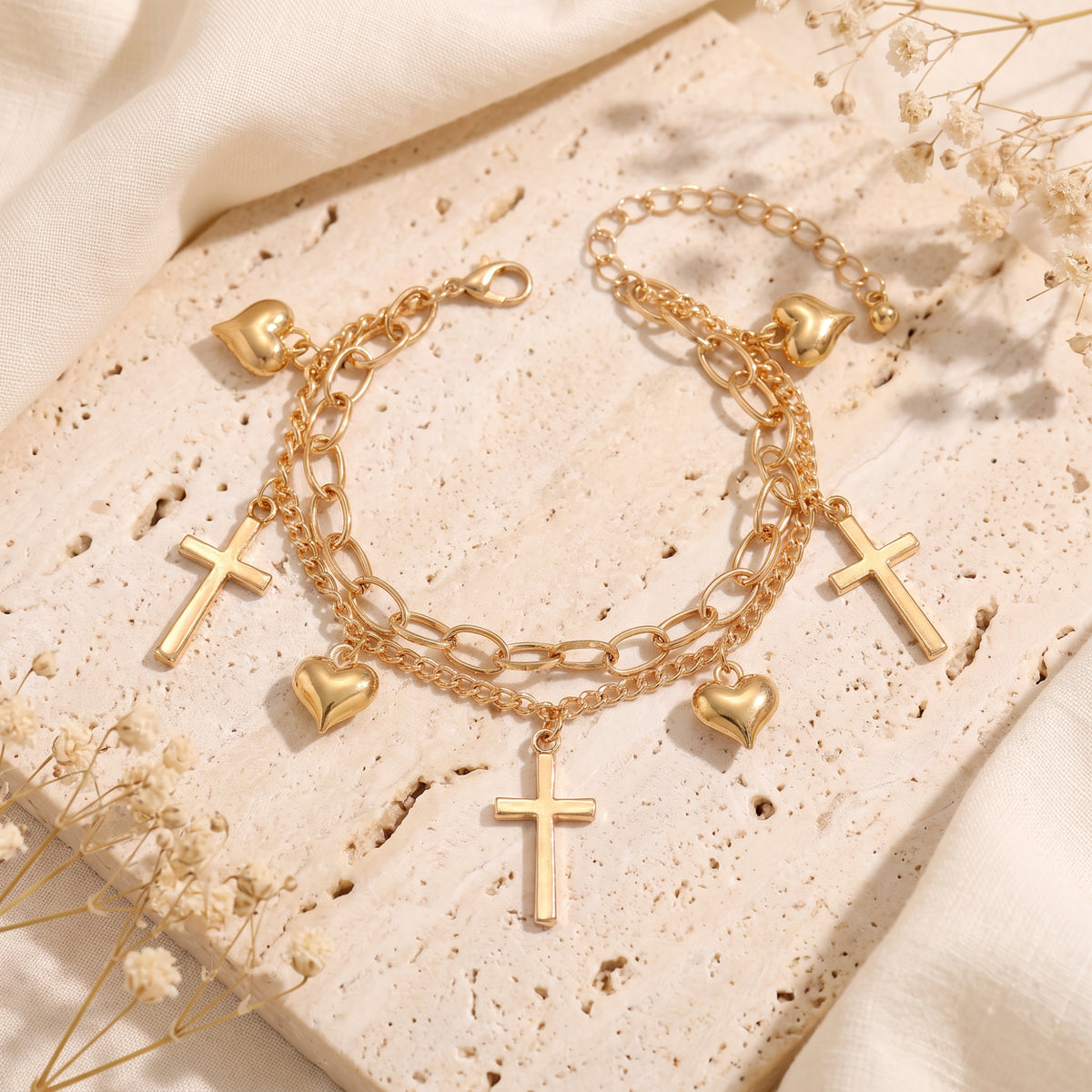 Top-down view of a gold-tone double-chain charm bracelet with heart and cross charms arranged in an oval.
