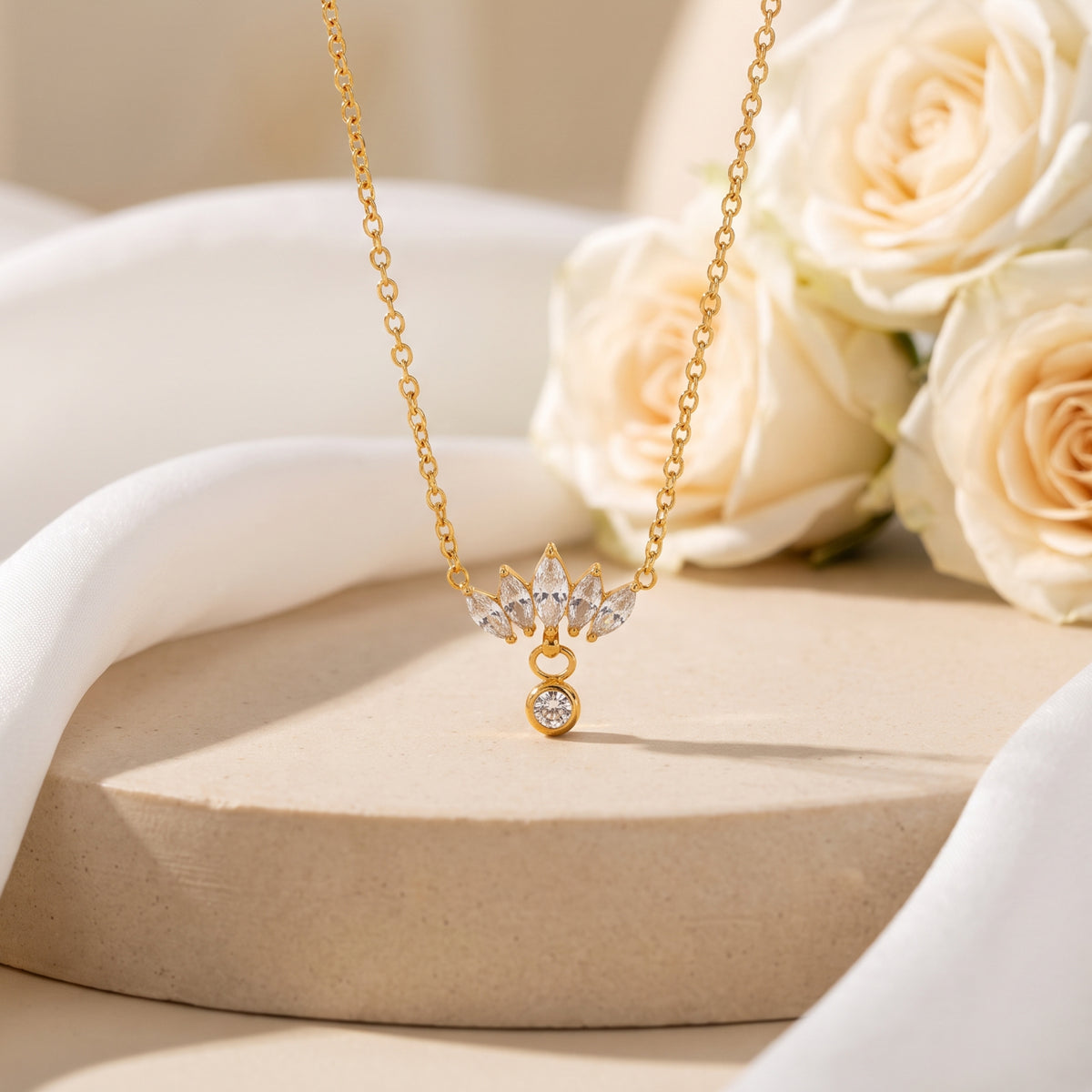 Front view of the gold-tone lotus cluster necklace hanging over a round pedestal with white roses.