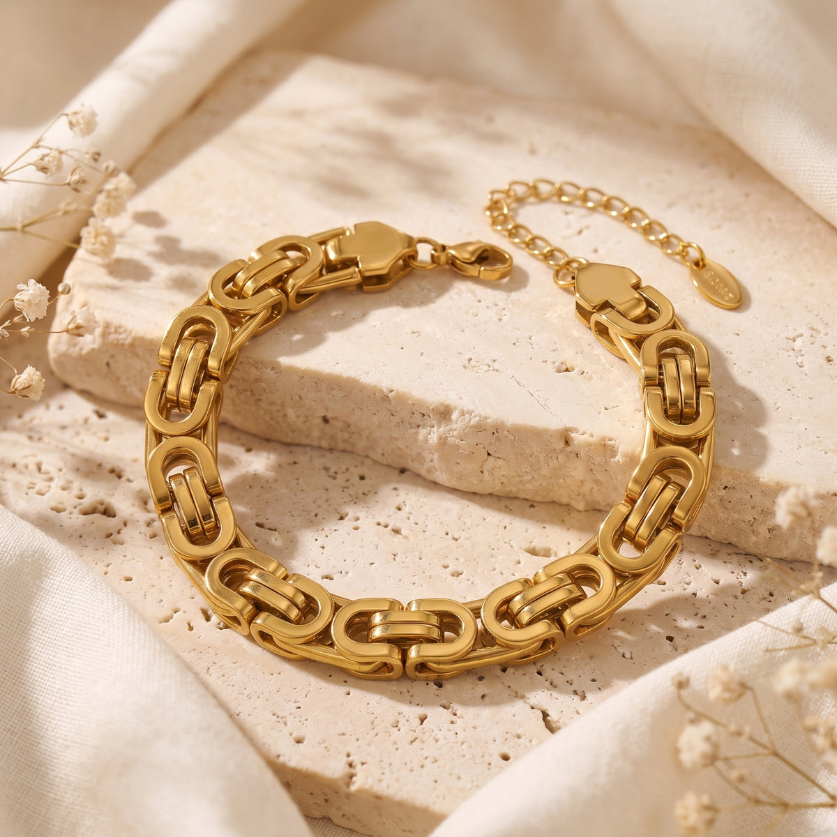 Gold-toned Byzantine link bracelet arranged on a raised beige stone block with cream fabric.