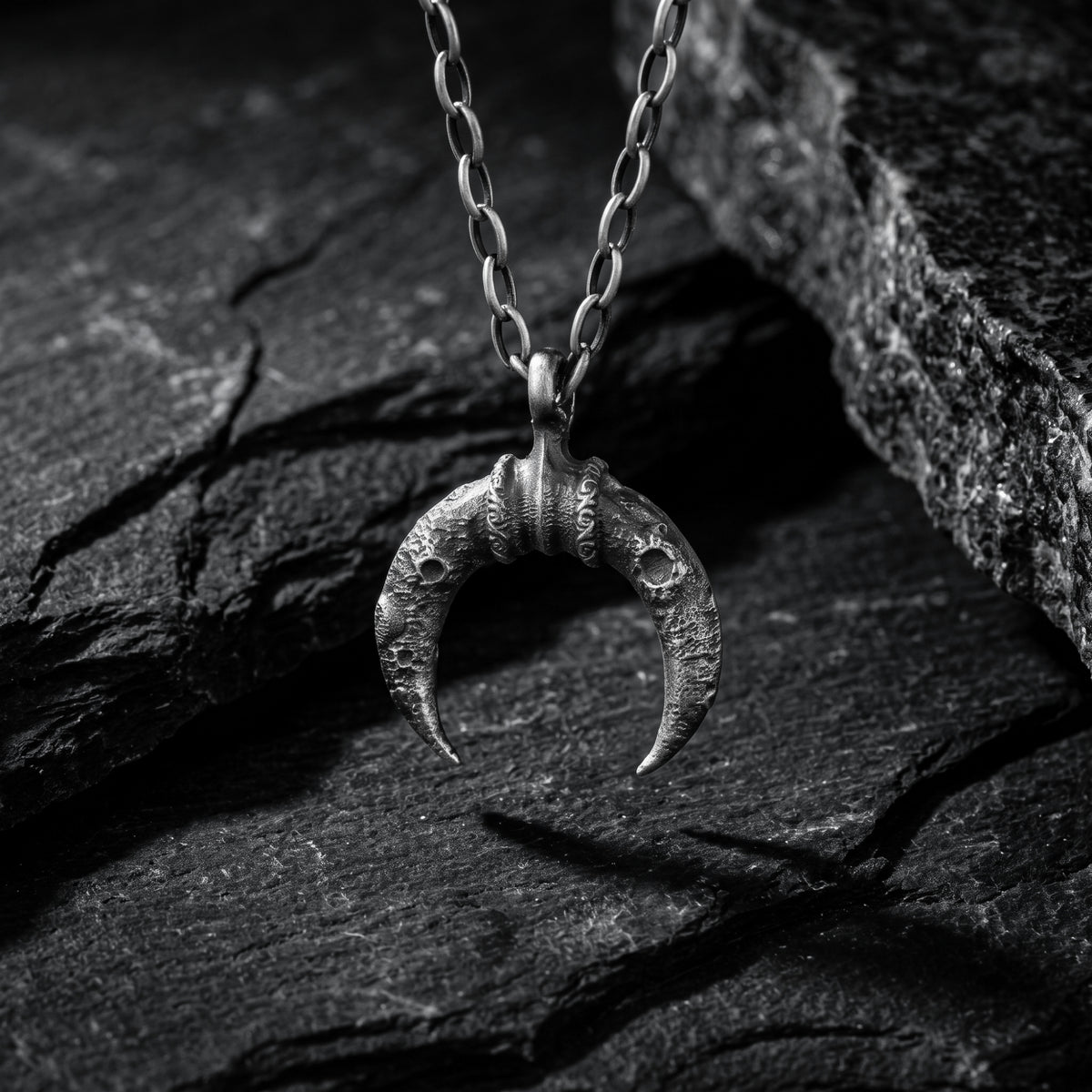 Textured antiqued silver crescent pendant hanging from its chain against dark slate.