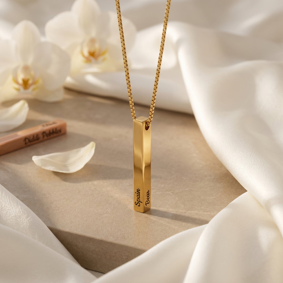 Close-up of a custom engraved gold bar pendant necklace on a stone surface.