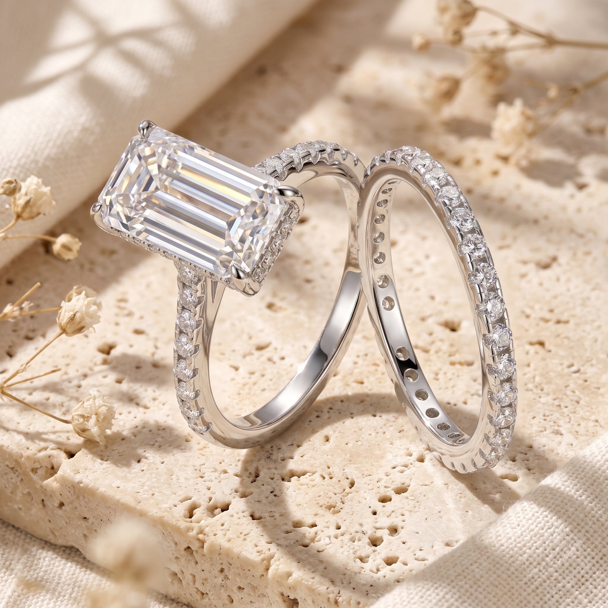 Close-up of the Alaria emerald-cut simulated diamond ring and eternity band on a neutral stone background.