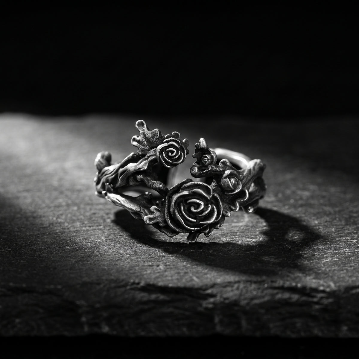Front studio view of the oxidized silver rose vine open ring resting on a textured dark slate surface.