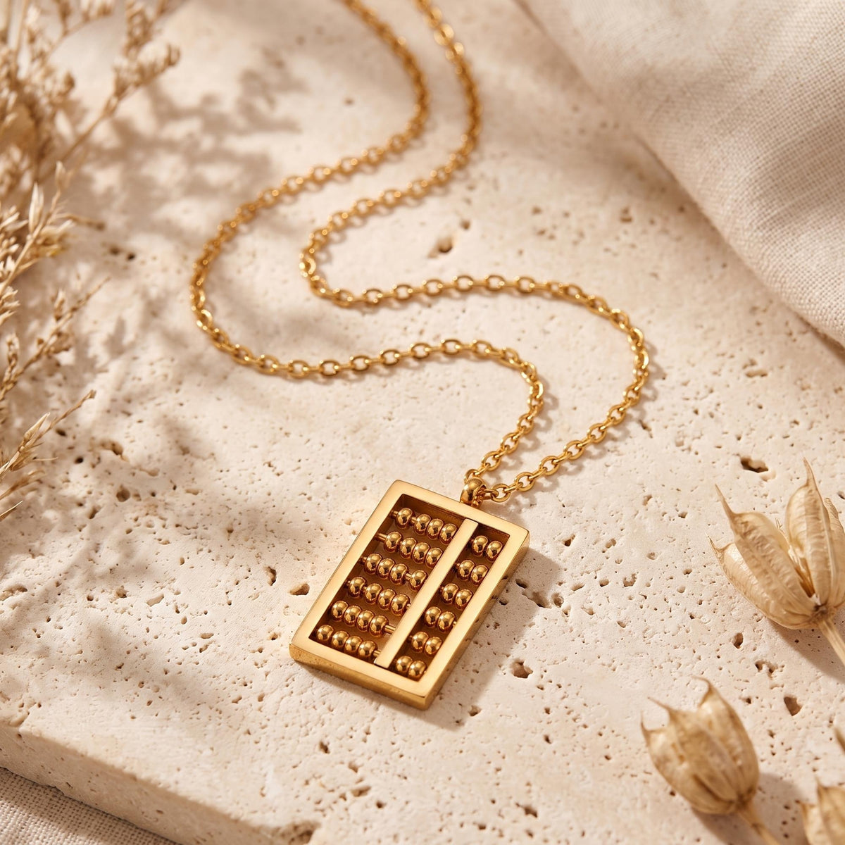 Gold-tone abacus pendant lying on a textured stone surface with its chain loosely coiled around it.