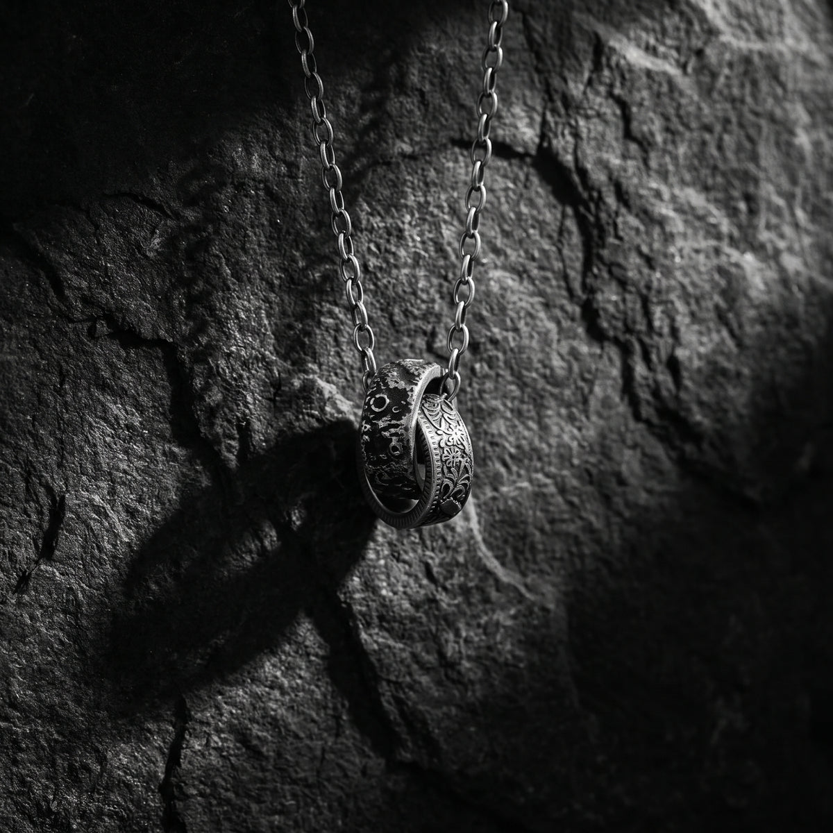 Detailed view of the interlocking lunar crater and floral silver rings hanging against dark stone.