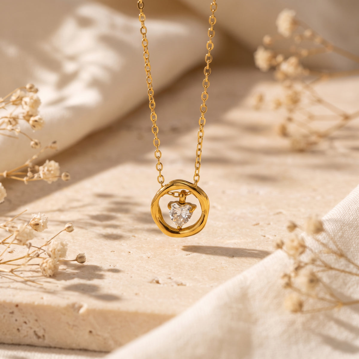 Gold-tone necklace hanging above a stone slab, with a clear heart-shaped stone suspended inside its circular pendant.