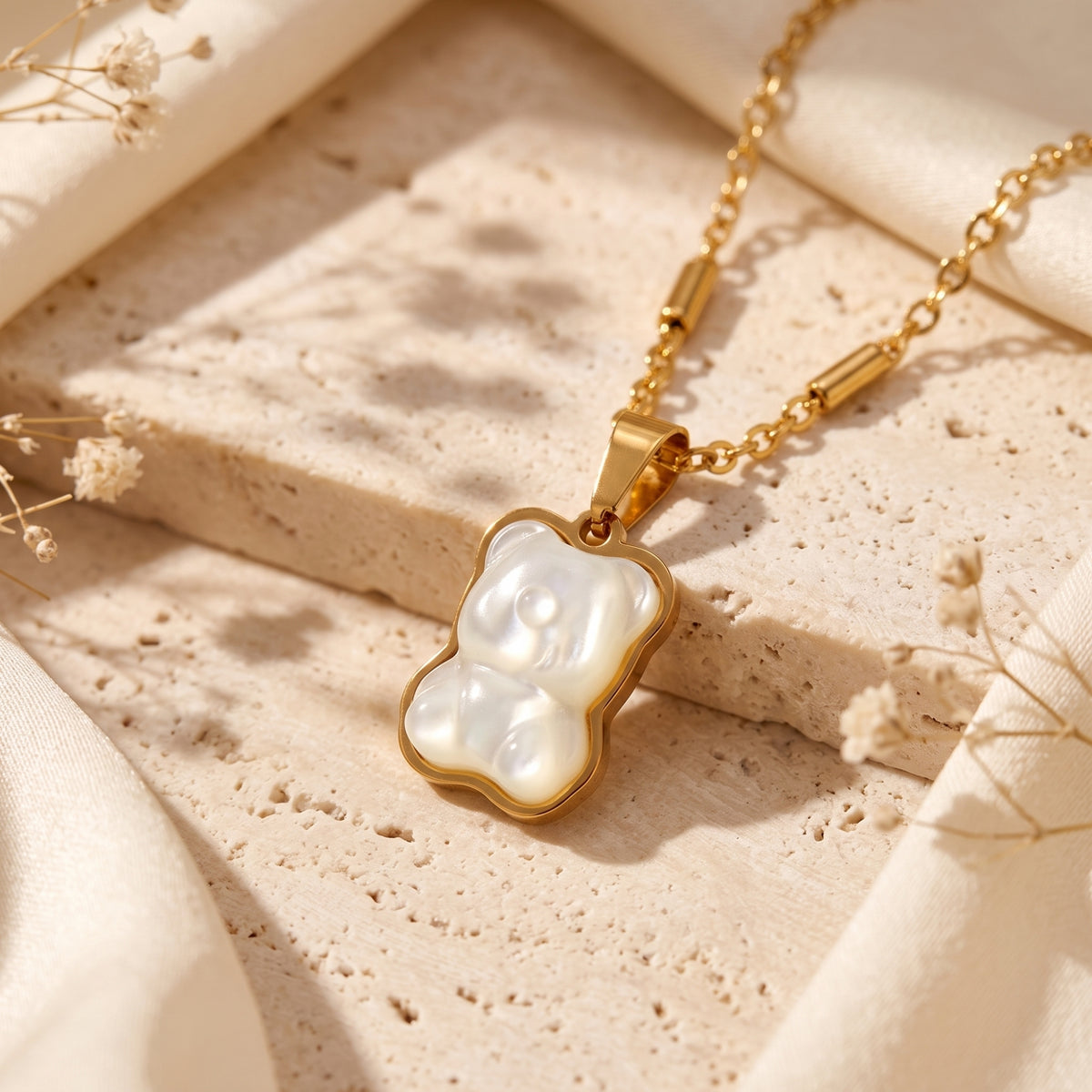 Angled close-up of the gold-tone bear pendant with a pearlescent inset on a textured stone surface.