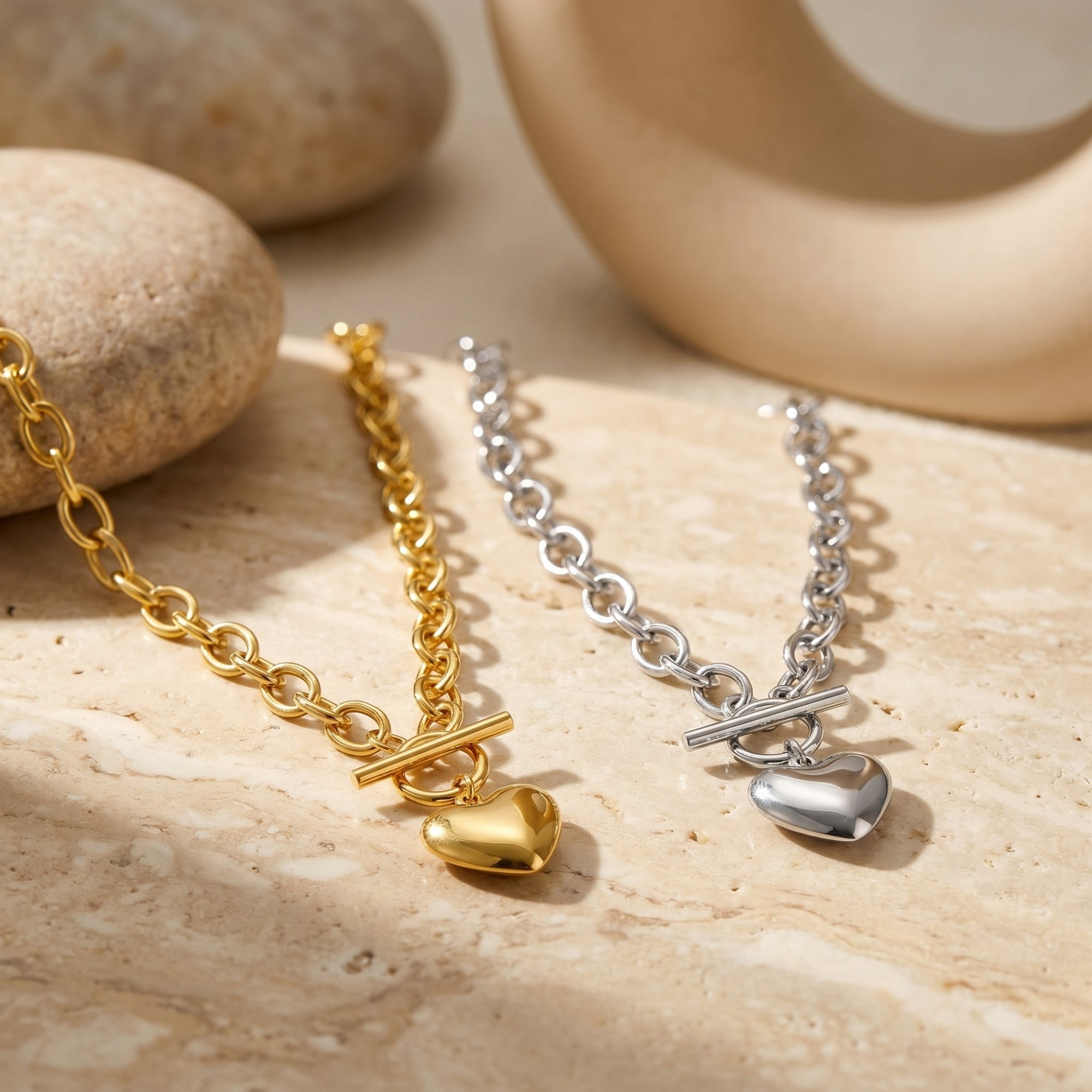 Gold and silver heart pendant necklaces displayed on a neutral stone background.
