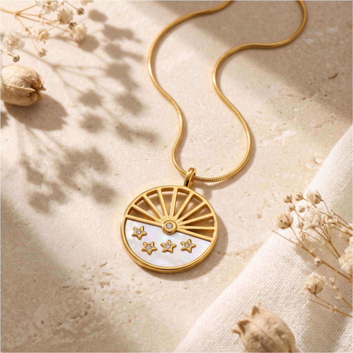 Flat-lay view of the gold-tone sunburst medallion pendant on textured stone near dried flowers.
