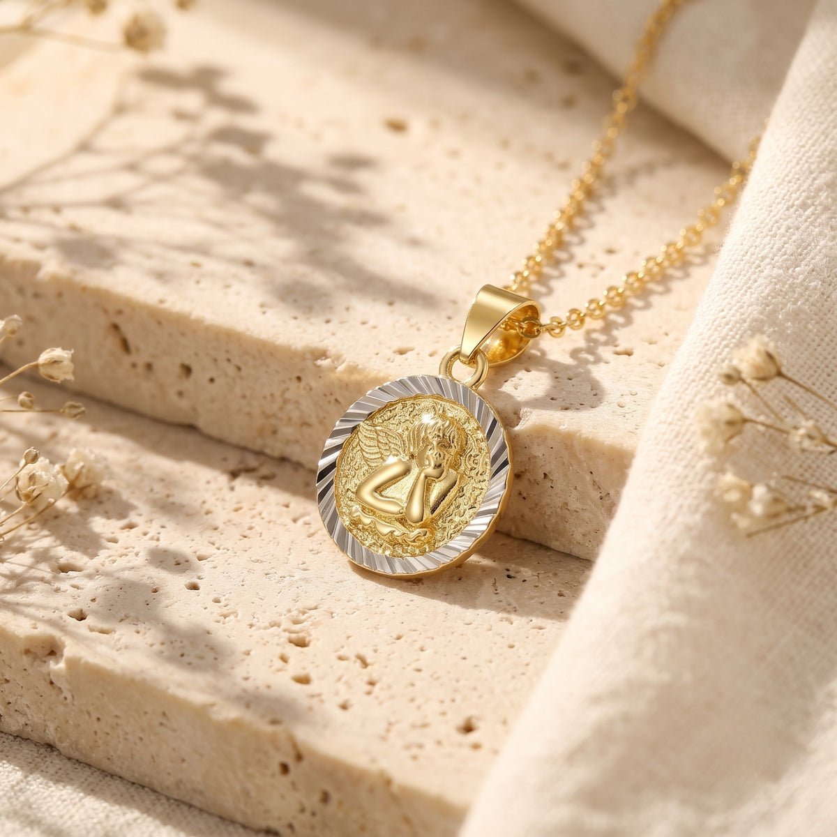 Angled close-up of a two-tone cherub medallion pendant and chain resting on porous stone blocks.