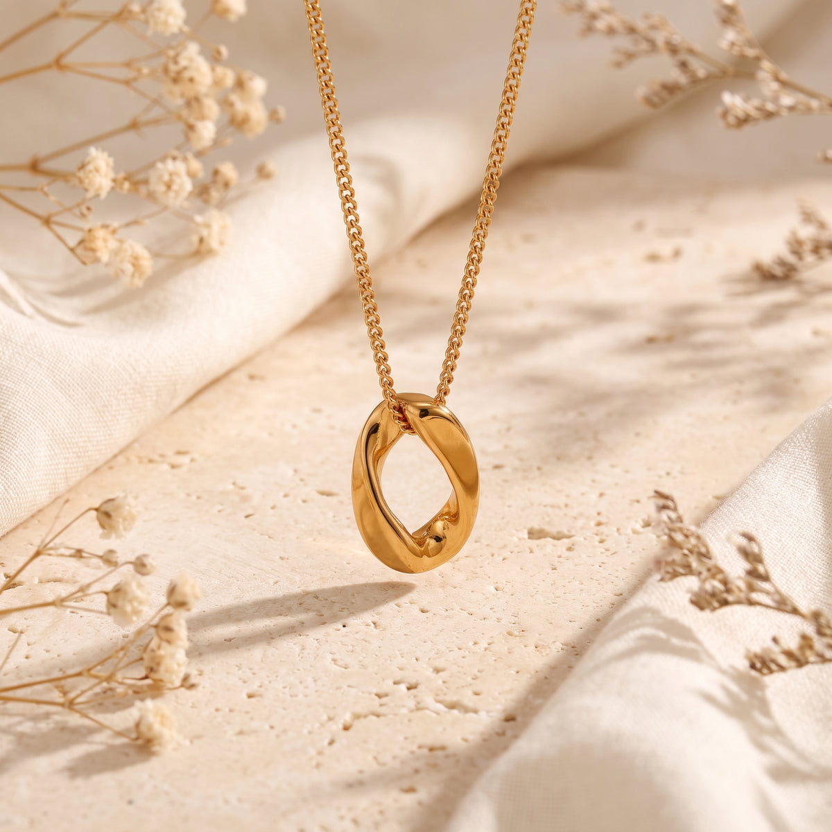 The gold-tone sculptural oval pendant suspended vertically above a neutral stone background.