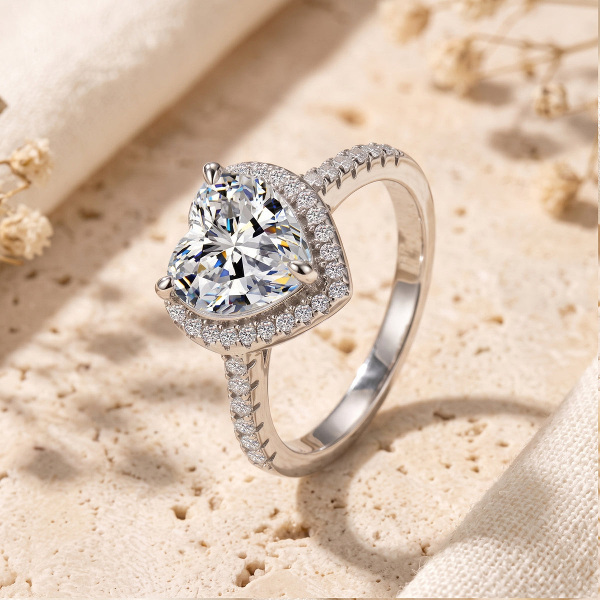Angled close-up of a silver heart-shaped halo ring with a simulated diamond standing on a stone surface.