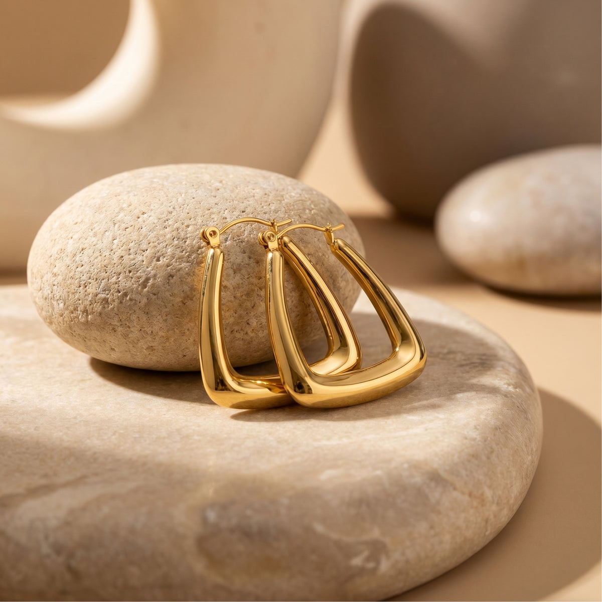 Gold 18K PVD stainless steel geometric hoops on a stone base.