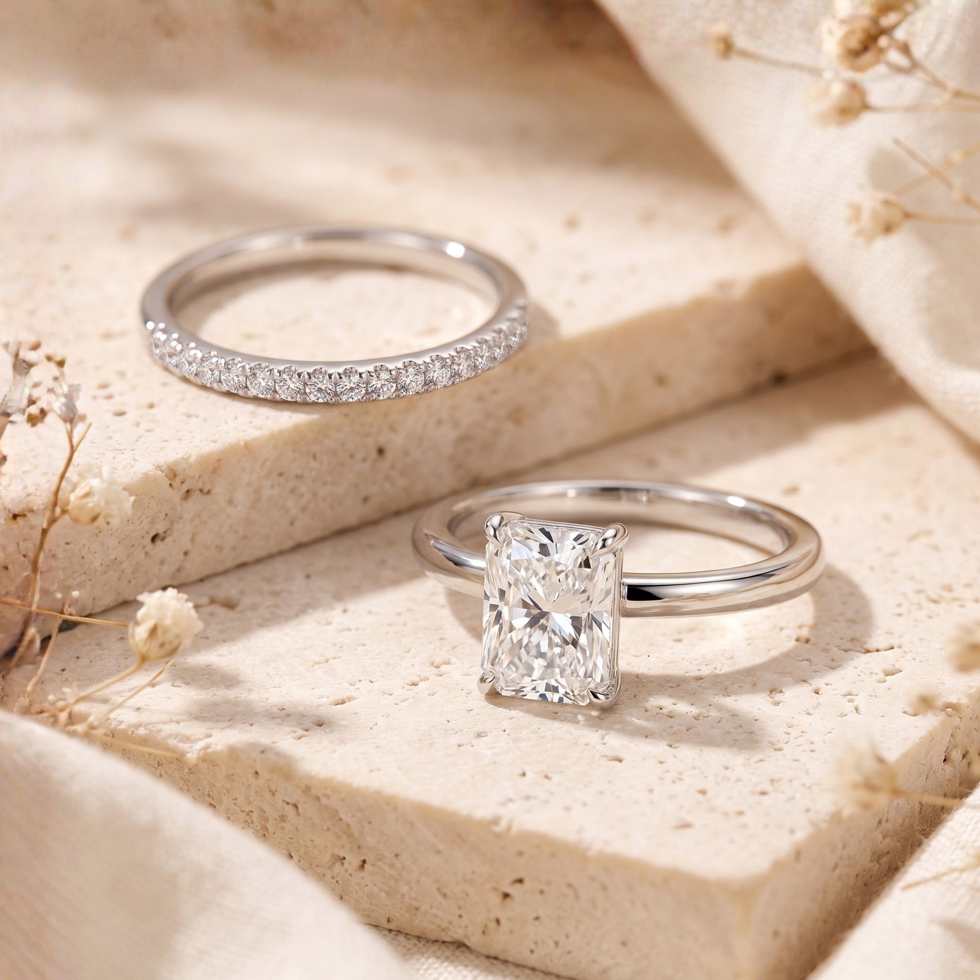 Close-up of emerald-cut simulated diamond and pavé band in sterling silver on textured stone.
