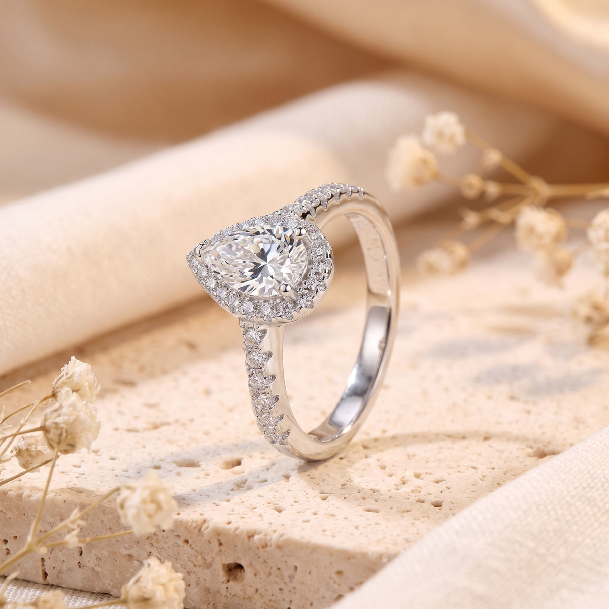 Side view of a silver pear-cut halo ring standing upright on a textured stone surface.