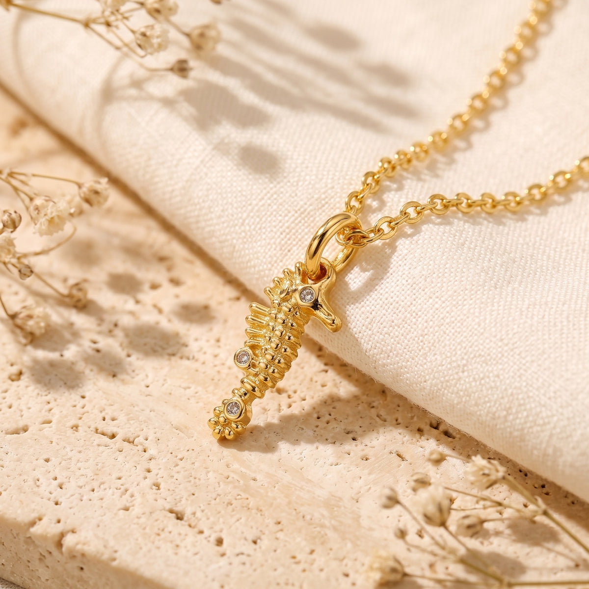 Angled detail of the gold-tone seahorse pendant with clear crystals on light fabric and stone.