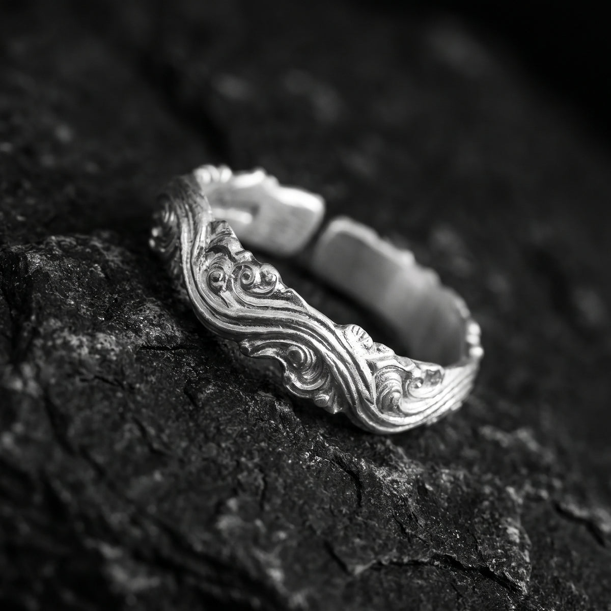 Angled macro view of the sculpted wave scroll ring showing its open back band on textured rock.