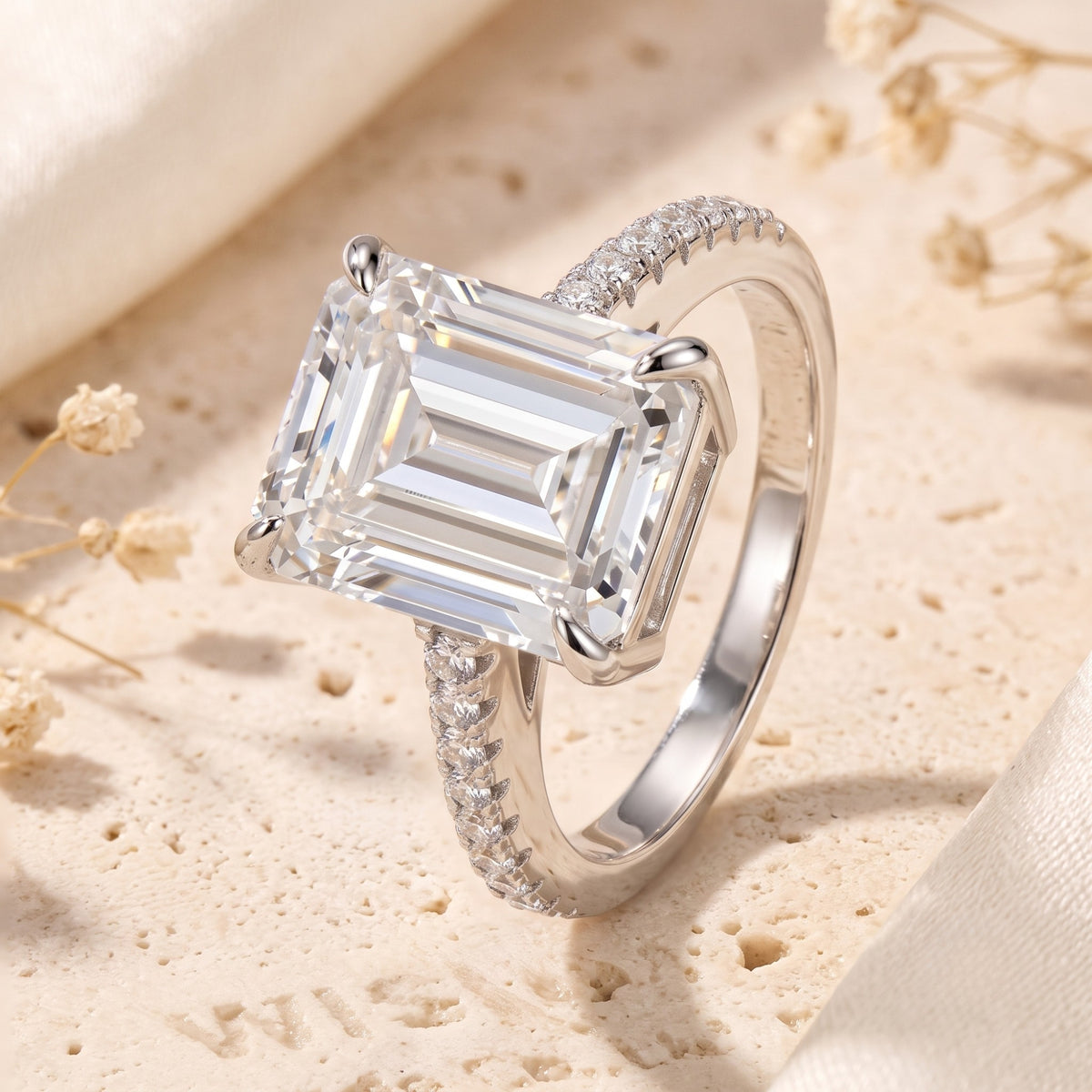 Three-quarter view of an emerald-cut solitaire ring resting on a textured stone surface, displaying its band and setting.