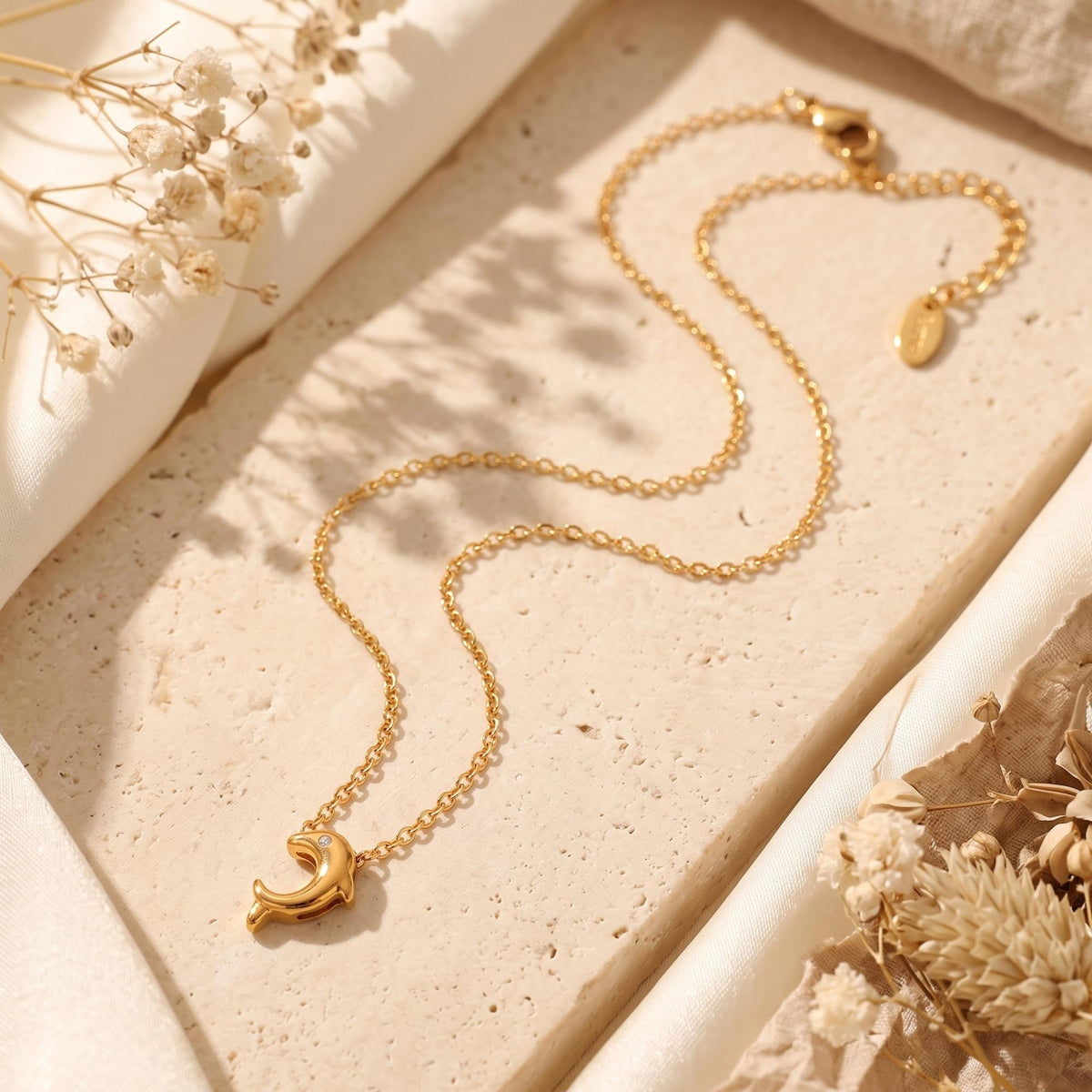 Full view of the gold-tone dolphin pendant necklace laid out on a textured stone surface.