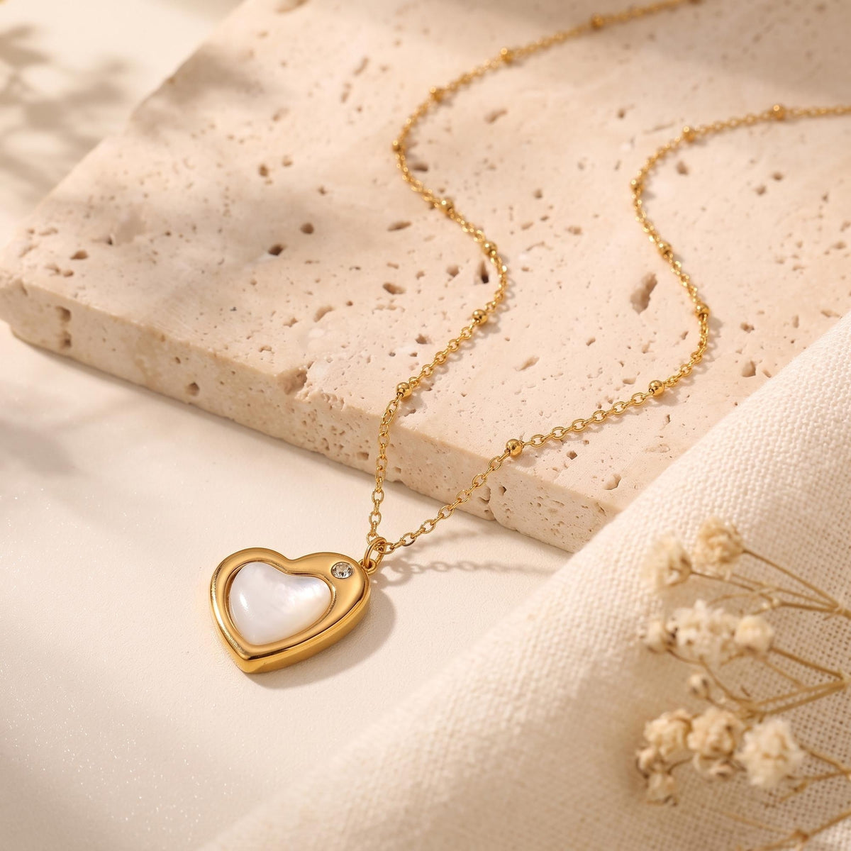 Gold-tone heart pendant necklace with a white mother-of-pearl style insert laid flat on a textured stone block.