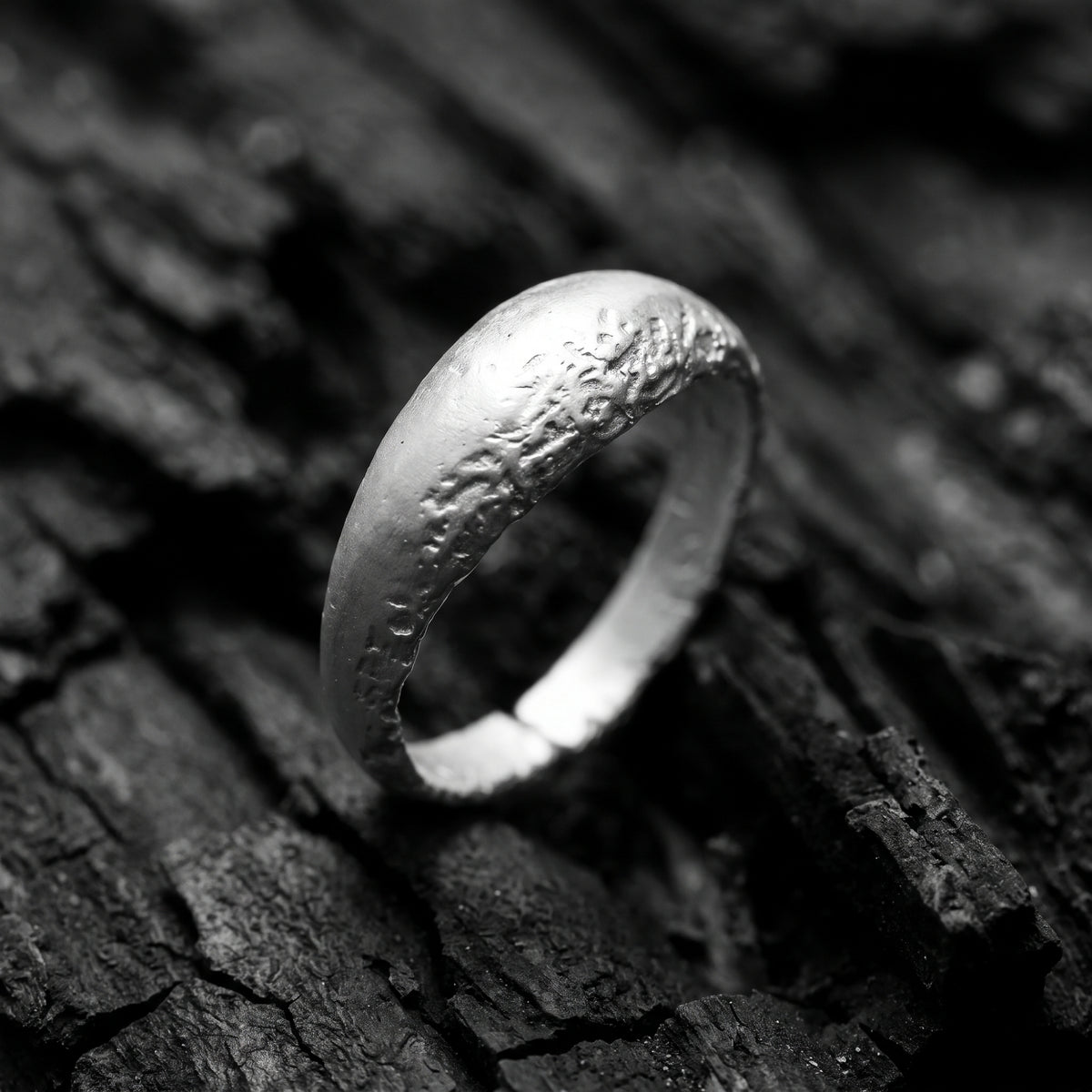 Angled close-up of a textured silver open-band ring standing upright on a dark textured surface.