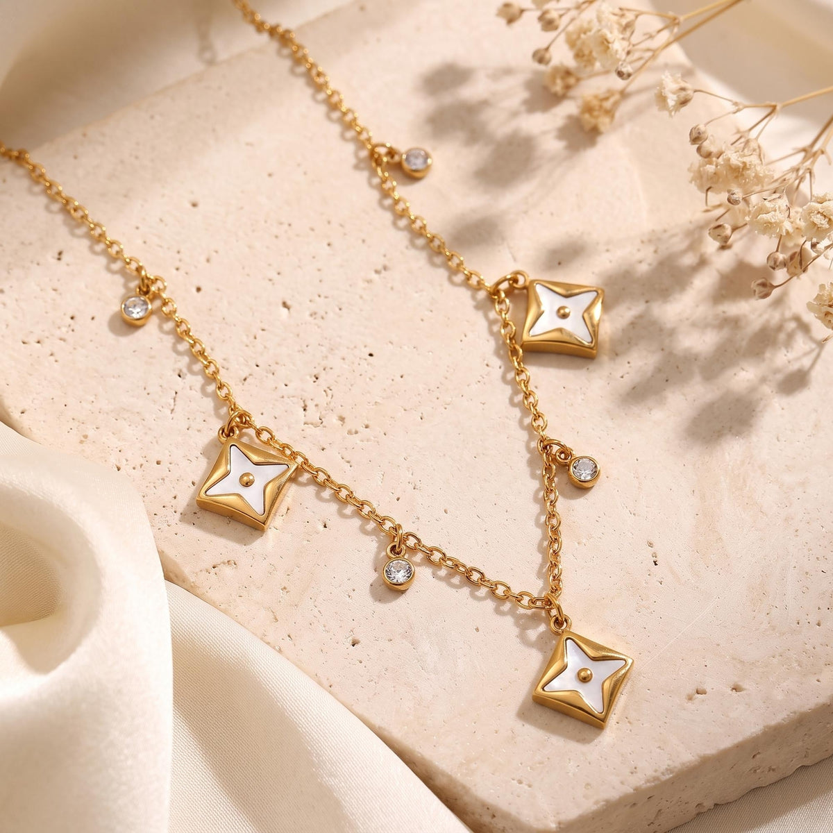 Close-up of gold star pendants with white inlays and brilliant-cut crystals on a textured stone surface.