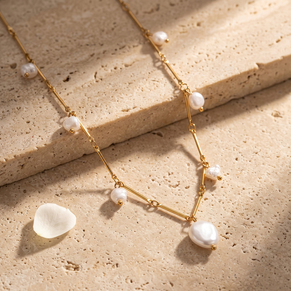 Detail shot of gold finish chain and irregular baroque freshwater pearls of the Henrietta necklace on stone.