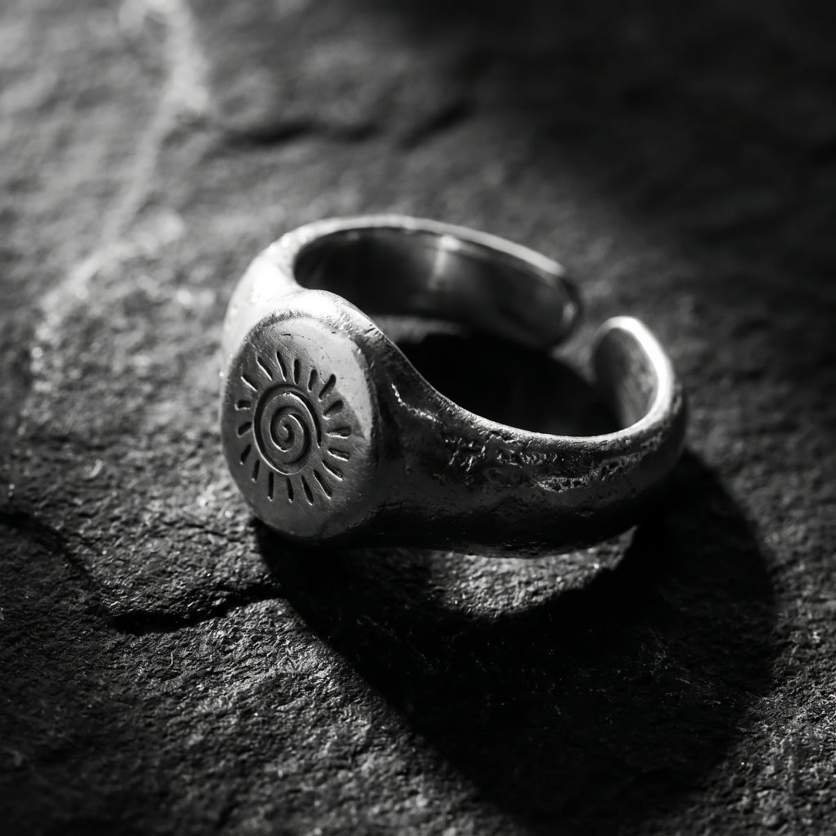 Angled close-up of the silver spiral sun signet ring on textured stone, showing its open band.