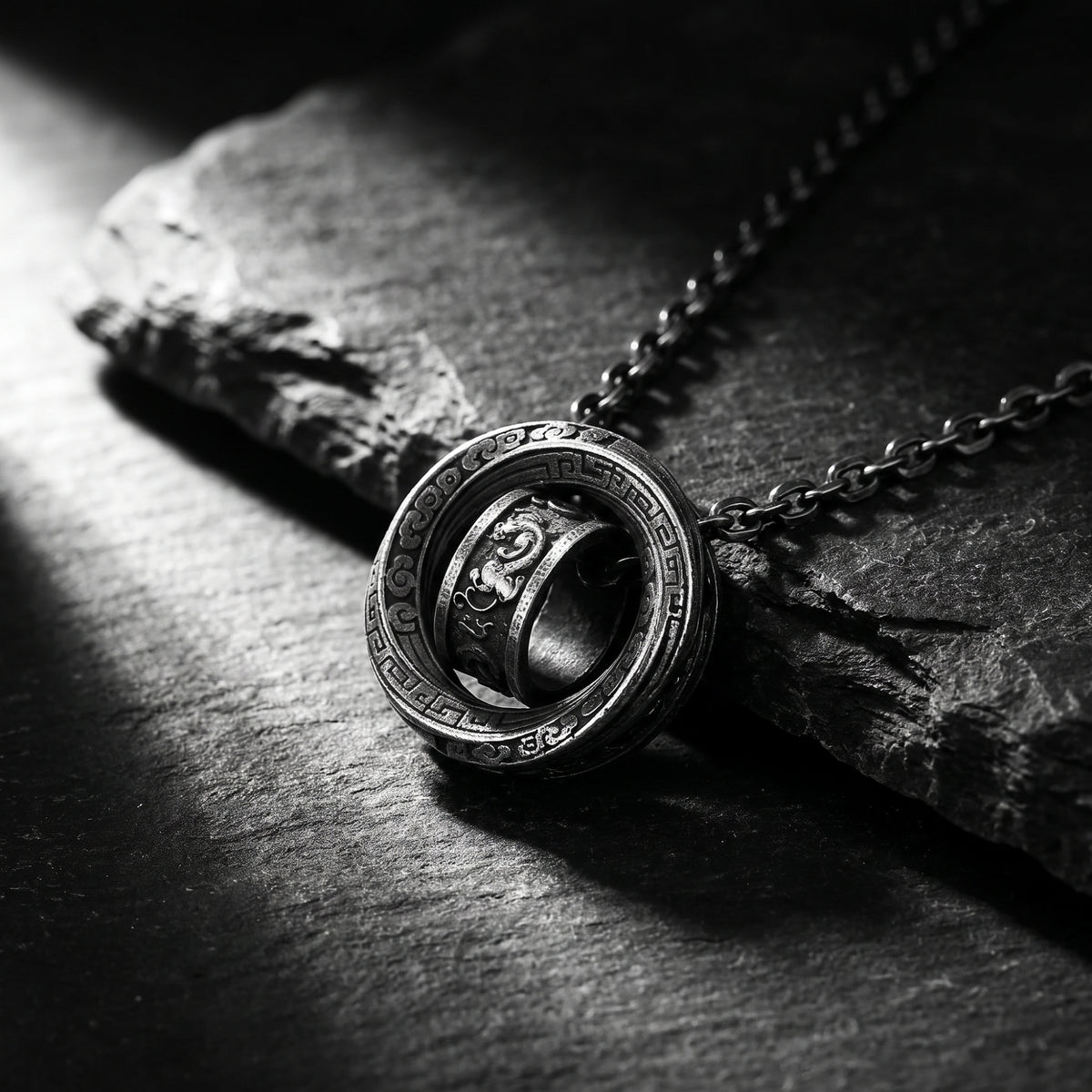 Angled close-up of the double-ring pendant resting against textured dark stone.
