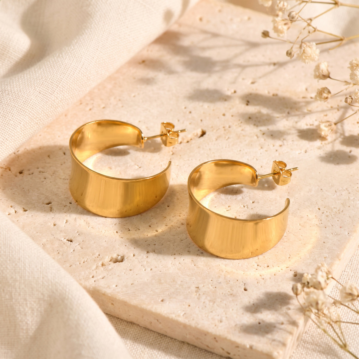 Pair of gold-tone flared hoop earrings lying on a stone slab with their post backings visible
